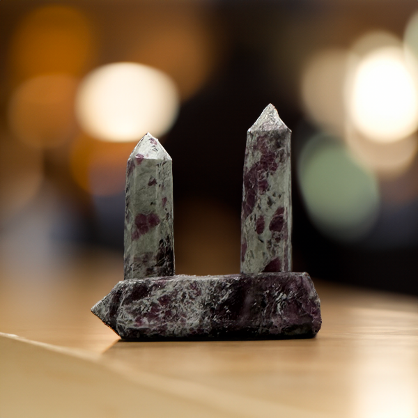 Two upright Pink Tourmaline towers with a base crystal on a wooden surface, soft bokeh lights in the background