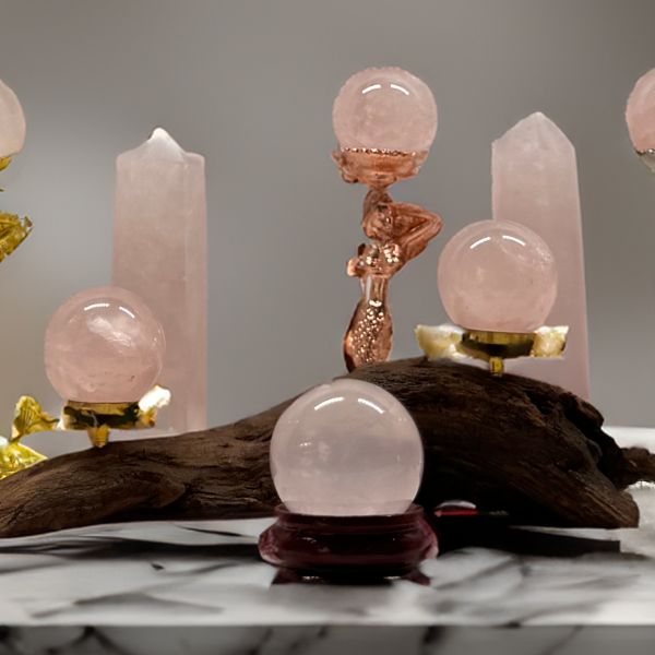Rose Quartz spheres displayed on artistic stands with a backdrop of upright Rose Quartz towers and golden accents on a marbled surface