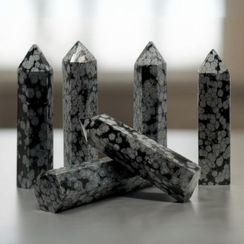 A collection of polished Snowflake Obsidian Towers arranged on a reflective surface, featuring distinctive snowflake-like patterns of gray on a black background.